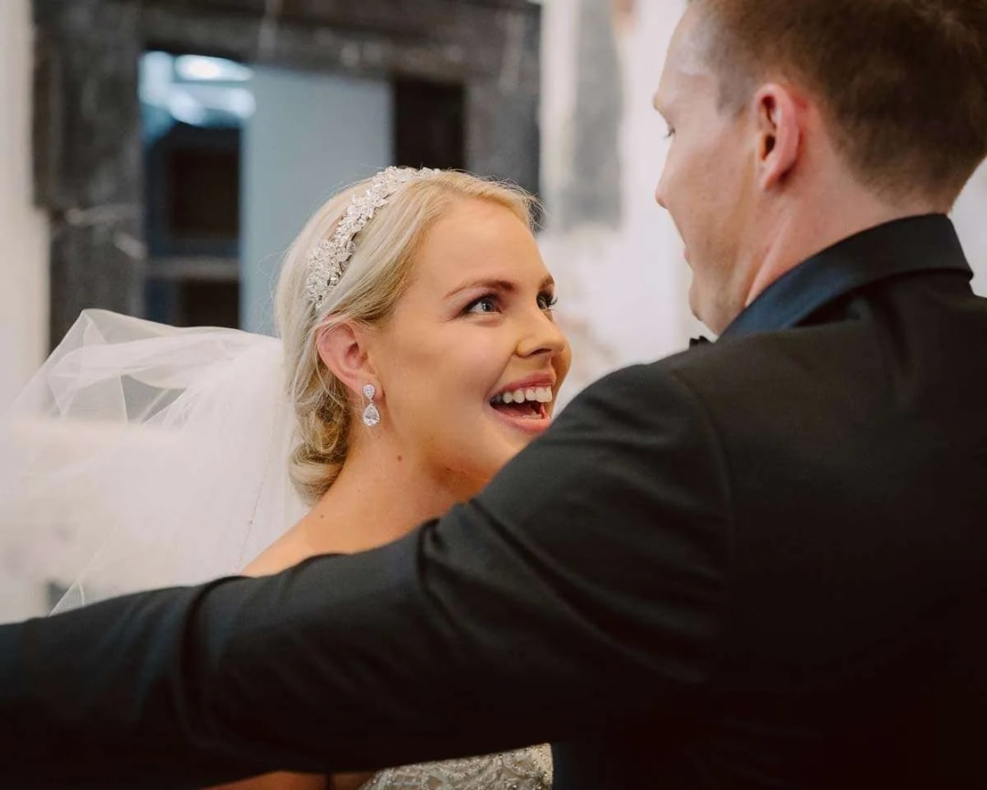 A bride and groom smiling at each other with joy inside a venue.