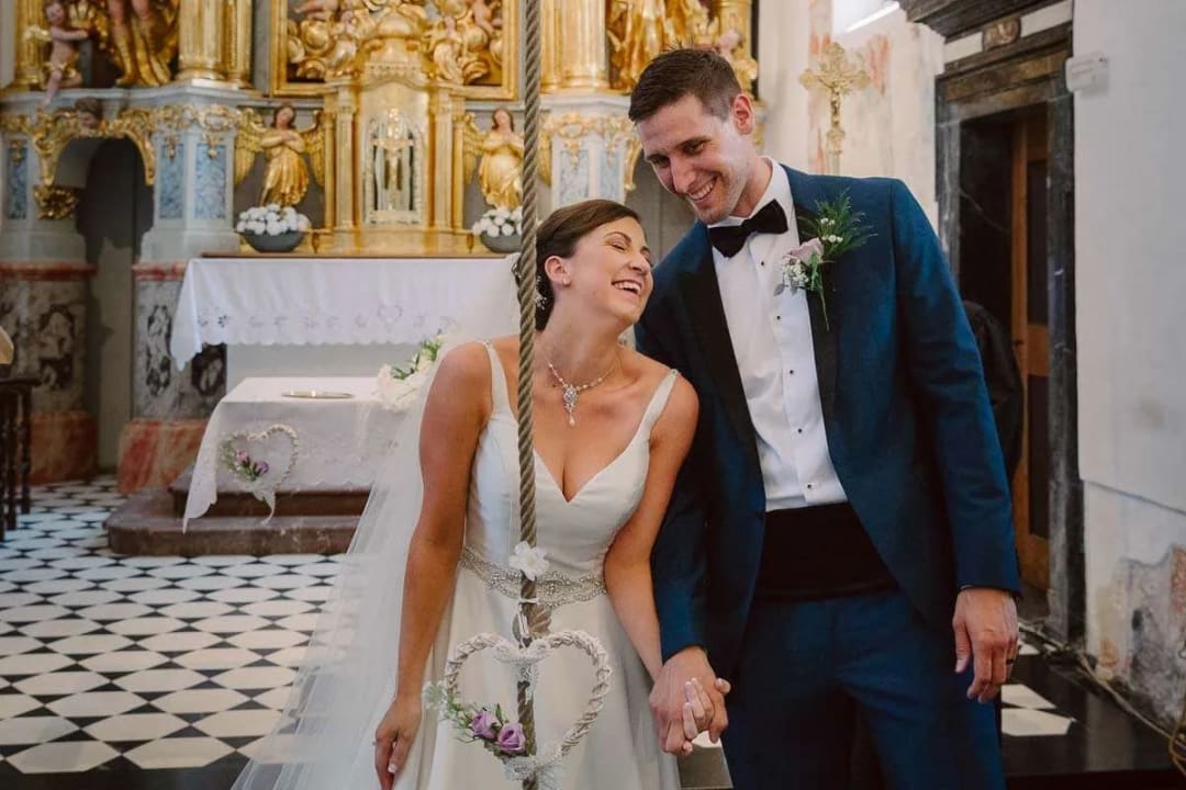 A bride and groom smiling and holding hands inside a beautifully decorated church during their wedding ceremony.