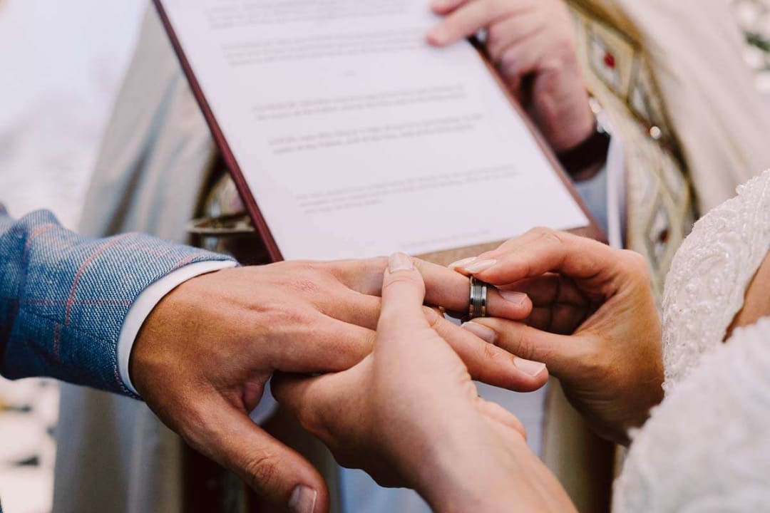 A close-up of a bride placing a ring on the groom's finger during their wedding ceremony.