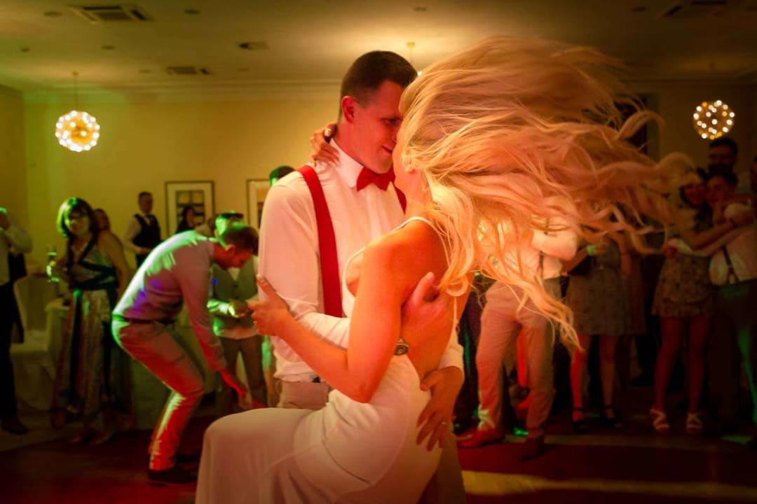 A couple dancing closely at a wedding reception, with the woman's hair flowing dramatically, surrounded by guests enjoying the event.