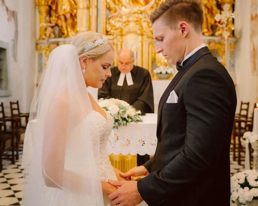 A bride and groom standing together, holding hands during their wedding ceremony in a beautifully decorated church.