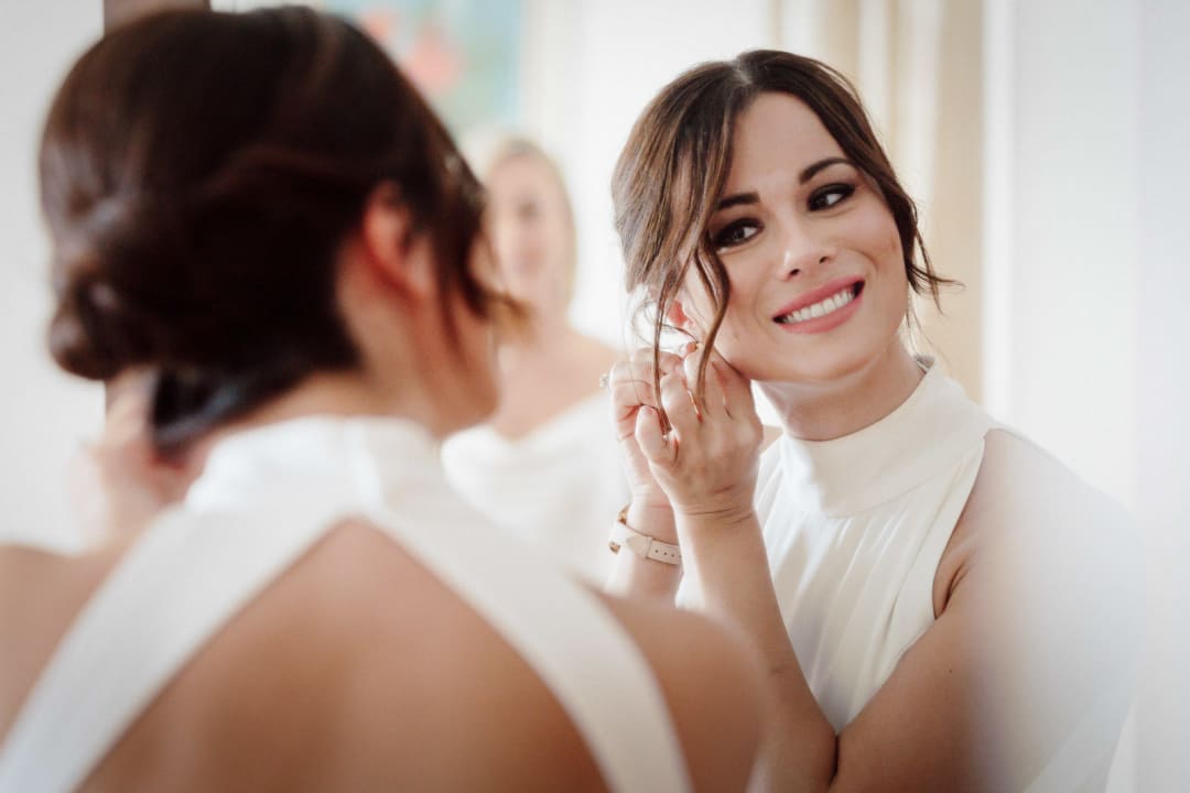 Bride adjusting earrings in the mirror during preparations.