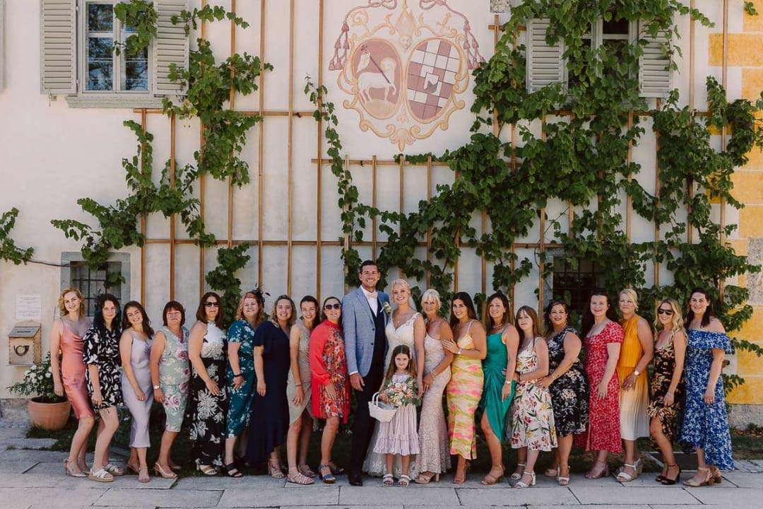 A group photo featuring a bride, groom, and wedding guests standing in front of a wall covered with green ivy.