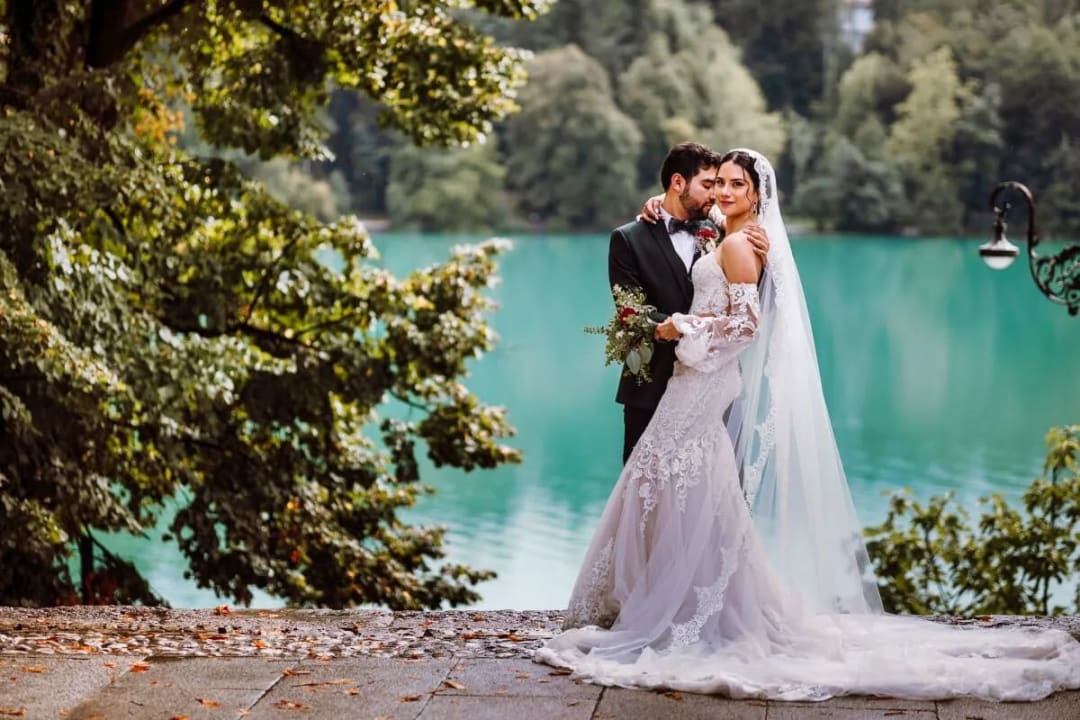 A bride and groom lovingly embrace near a scenic lake, surrounded by lush greenery.