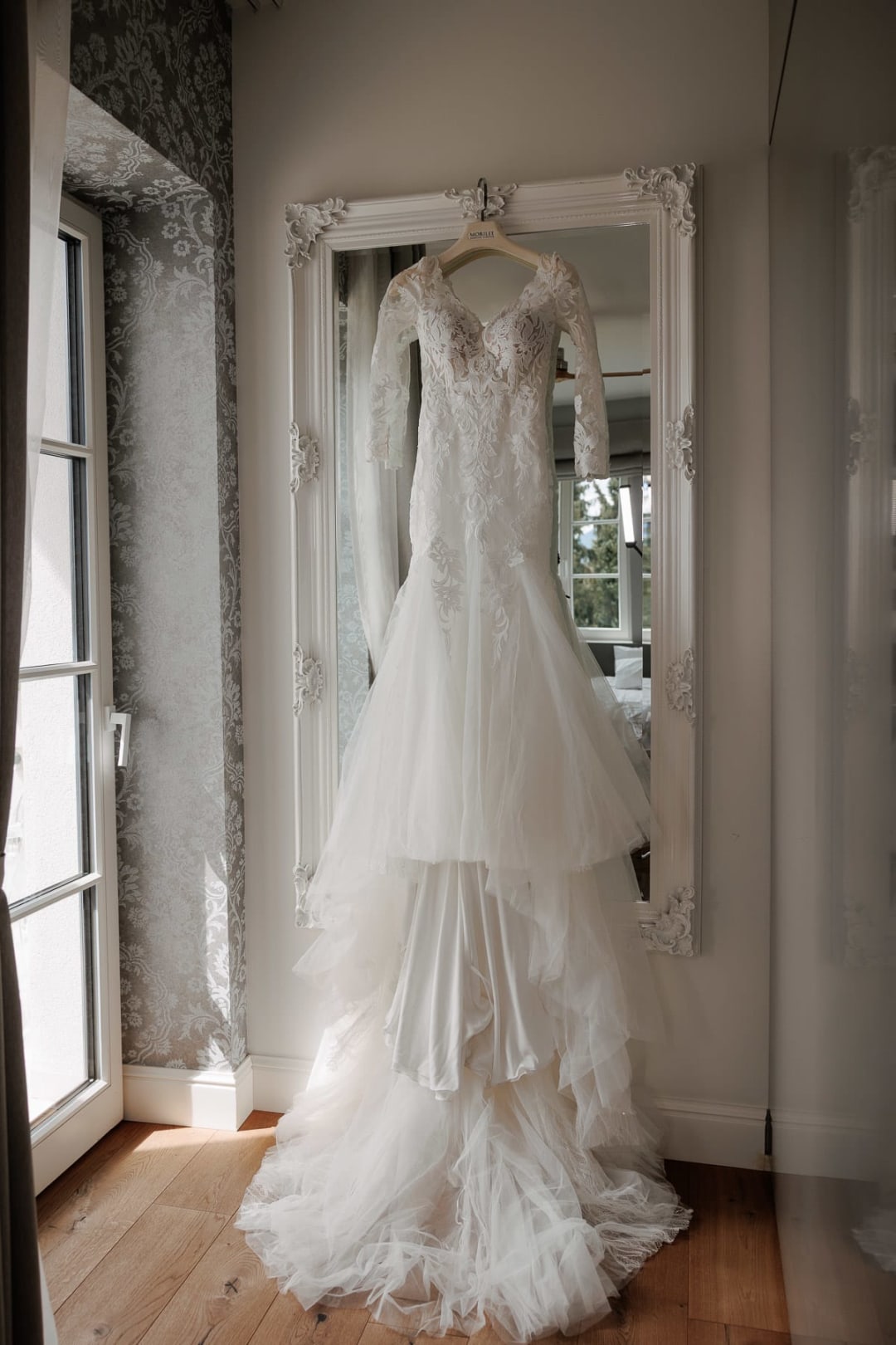 	Elegant lace wedding dress hanging in a bright window before the ceremony.