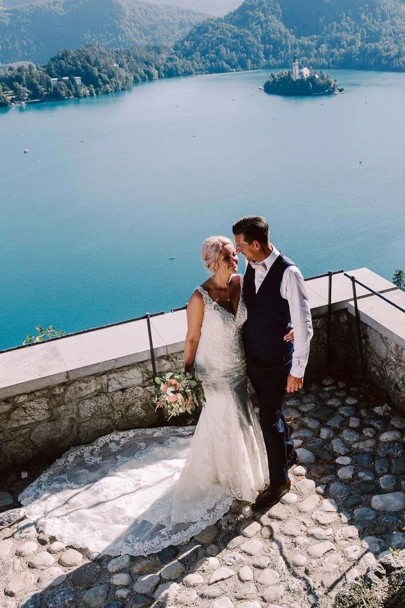 A bride and groom smiling at each other with Lake Bled and the iconic island church in the background.