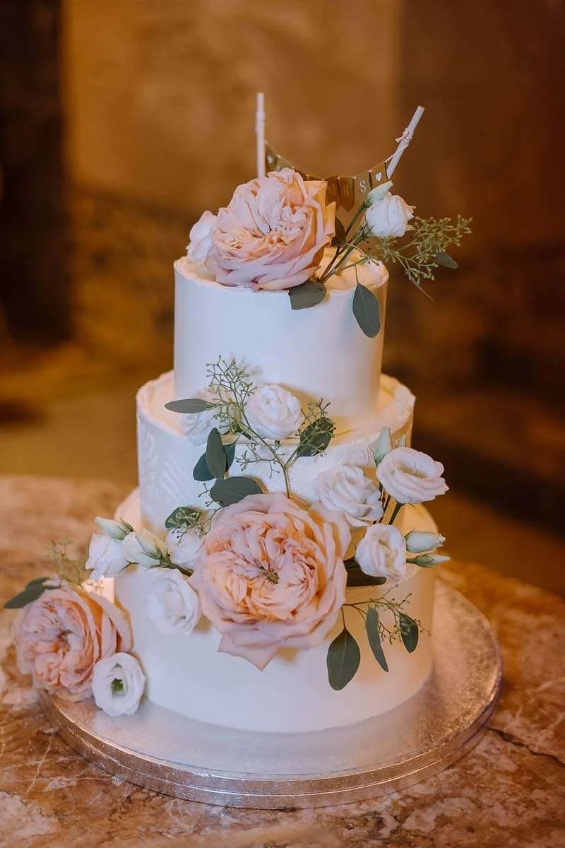 A three-tiered wedding cake adorned with pink and white flowers, set against an elegant background.