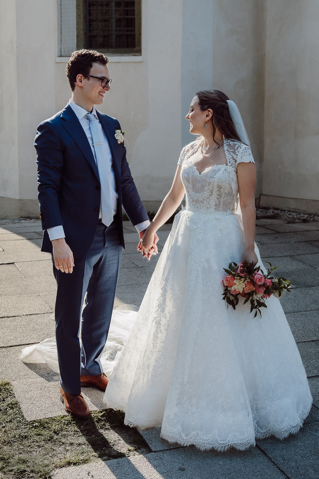 Elegant bride and groom walking together at Lake Bled after their wedding ceremony, photographed in a timeless editorial style.