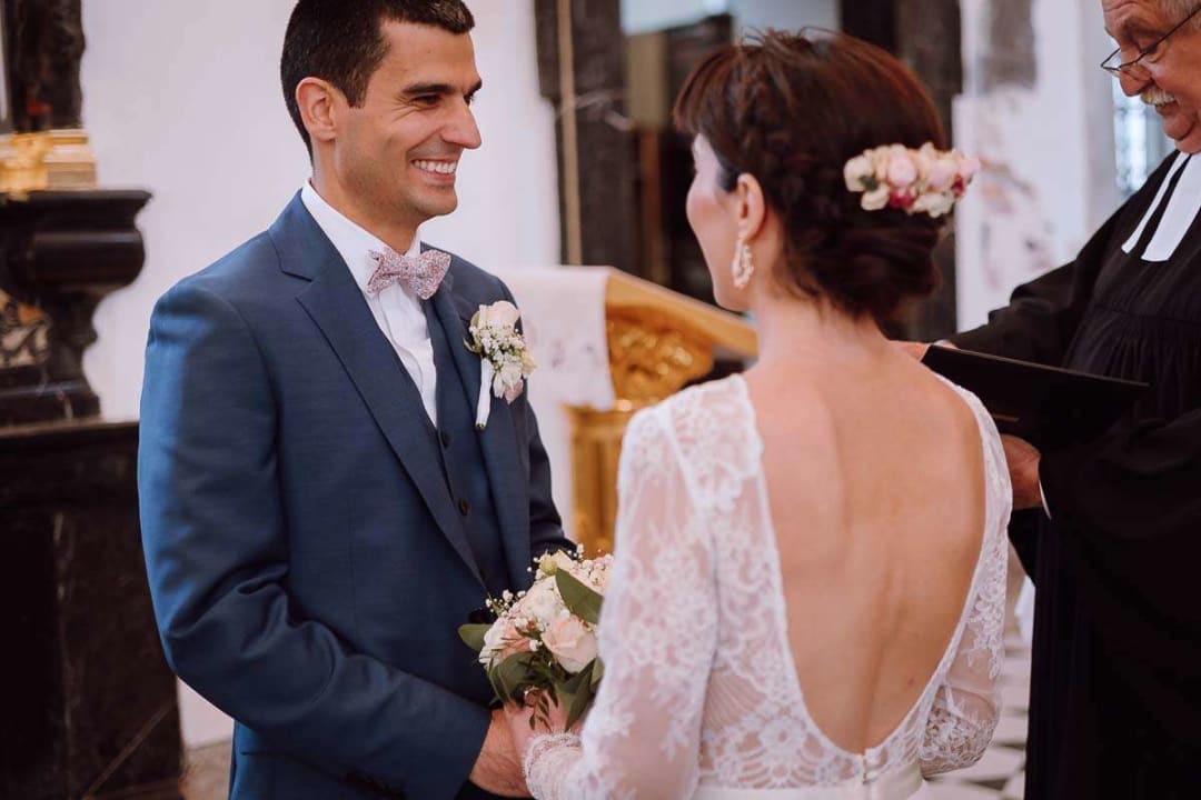 A bride and groom smiling at each other as they exchange vows during their wedding ceremony inside a church.