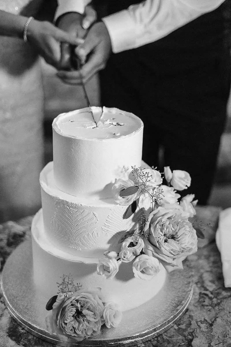 A bride and groom cutting a three-tiered wedding cake decorated with flowers.