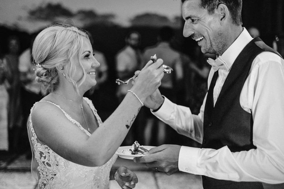 A bride and groom smiling and feeding each other cake during their wedding reception.