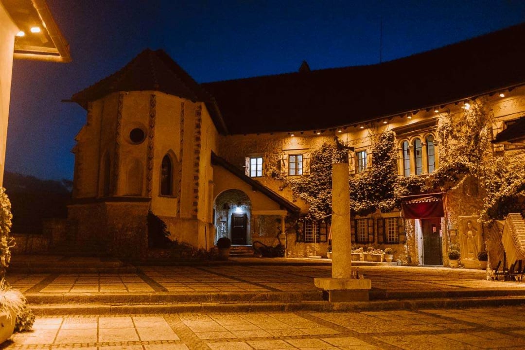 The illuminated courtyard of a historic castle at night, with ivy covering the walls and warm lights glowing from the windows.