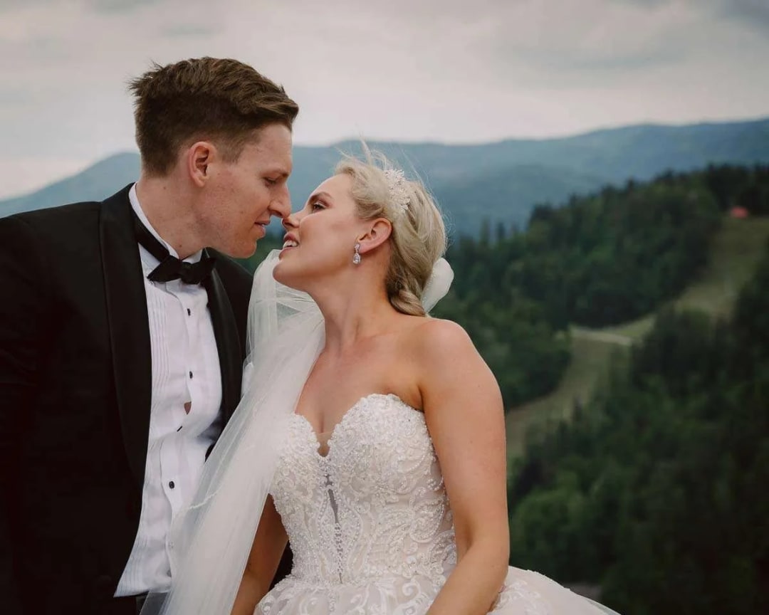 A bride and groom about to kiss with a scenic view of mountains in the background.