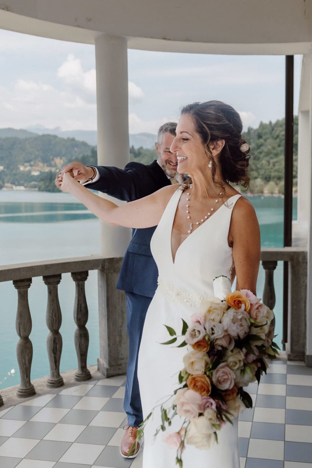 Wedding first look at Lake Bled with the bride turning around to reveal the wedding dress on a lakeside terrace.