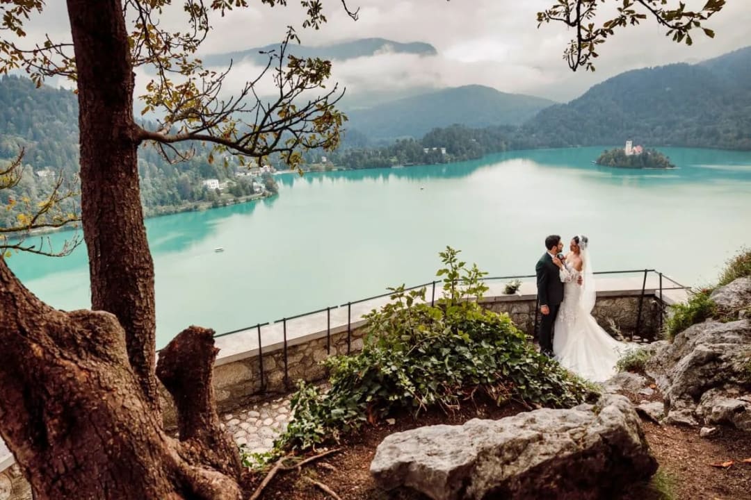 A bride and groom standing together overlooking the serene Lake Bled with its iconic island and church in the distance.