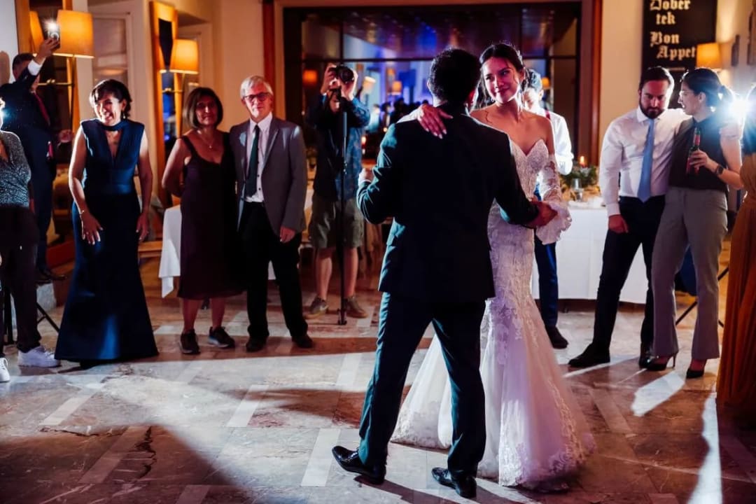 A bride and groom share their first dance at a wedding reception, surrounded by applauding guests.
