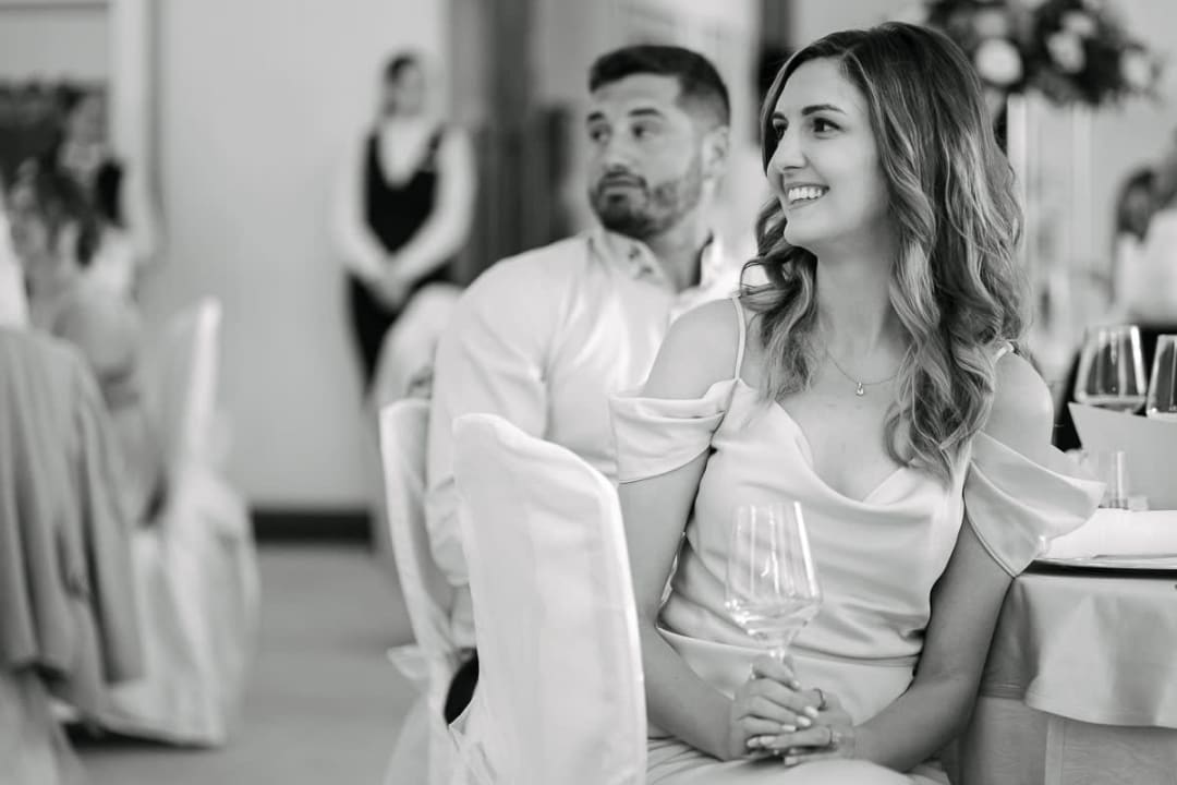 A woman in a formal dress smiling while holding a glass at a wedding reception.