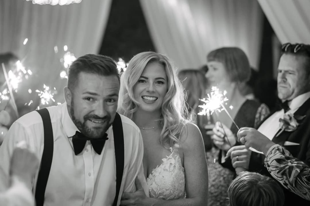 A joyful bride and groom surrounded by guests holding sparklers during a wedding celebration.