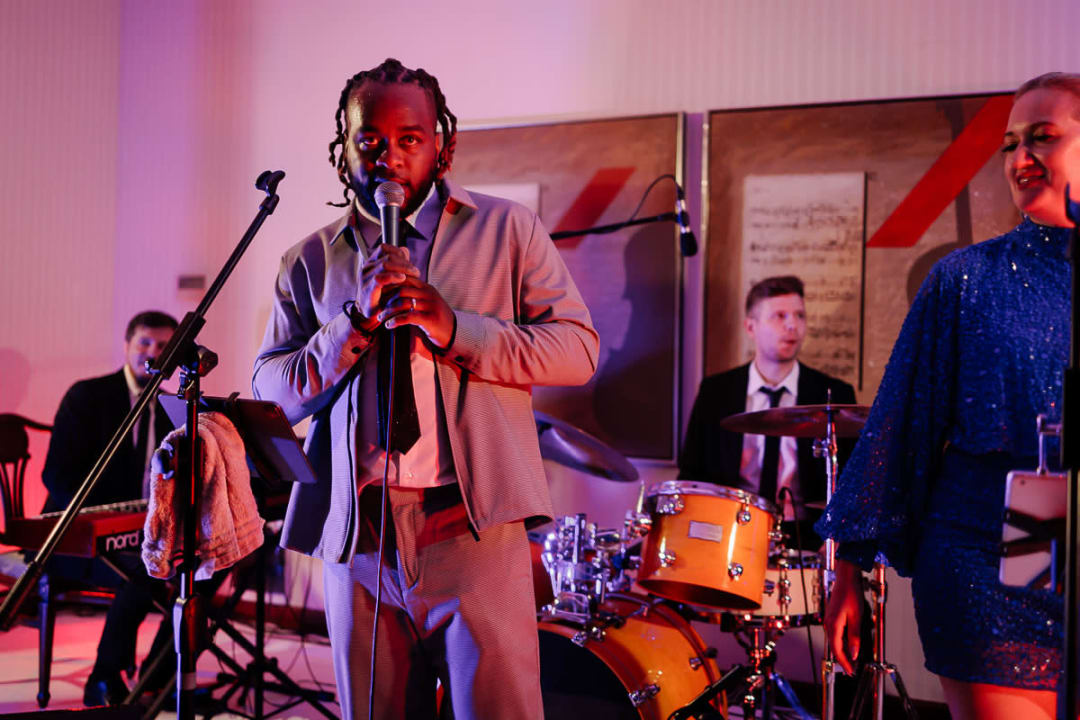 A band performing at a wedding reception with a man singing into a microphone, accompanied by a keyboard player and a drummer.
