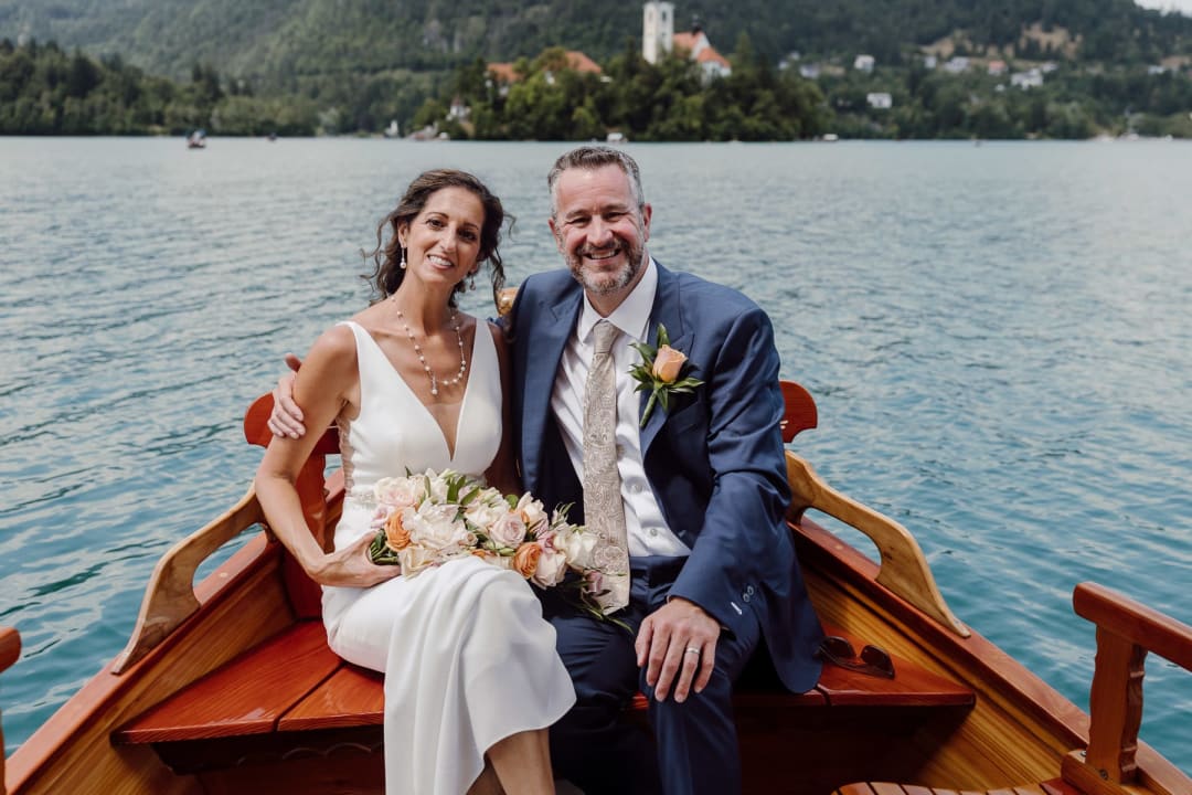 Newlyweds sitting together in a wooden boat on the lake.