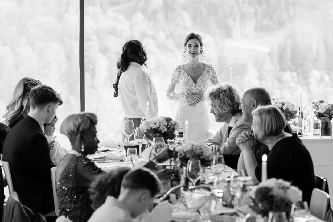 Black and white wide shot of the wedding reception in full swing, guests gathered around the tables.