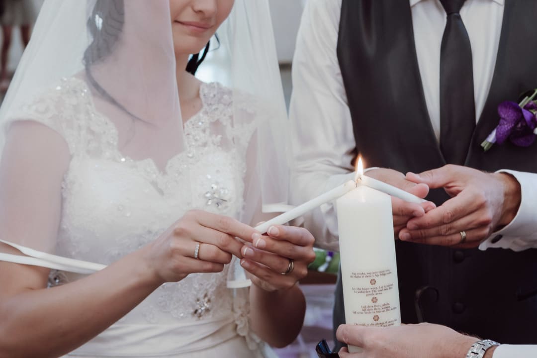 Bride and groom lighting a wedding candle during a religious ceremony at a Lake Bled wedding, photographed in a refined editorial style.
