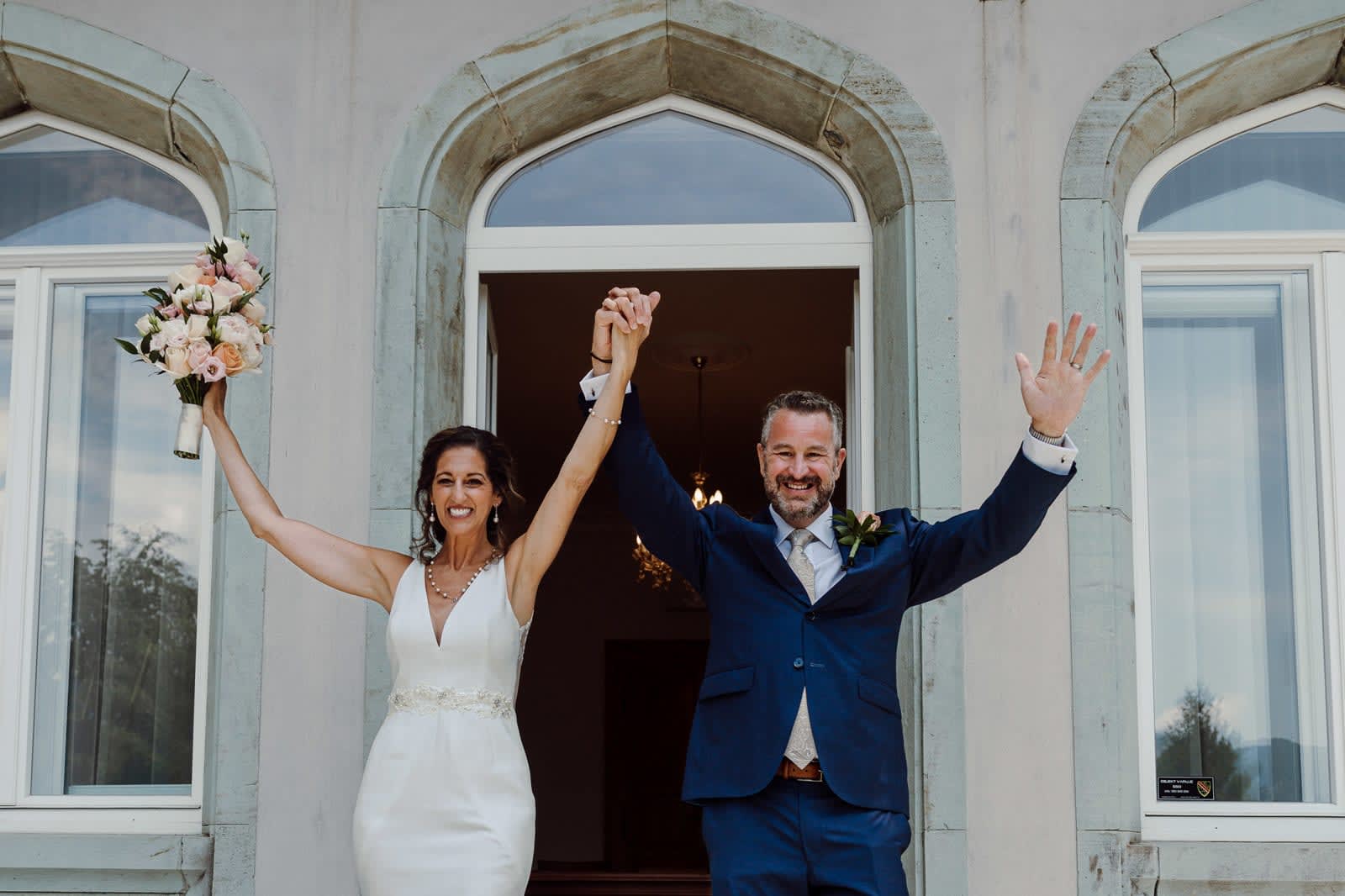 Just-married couple celebrating outside the venue with raised hands.