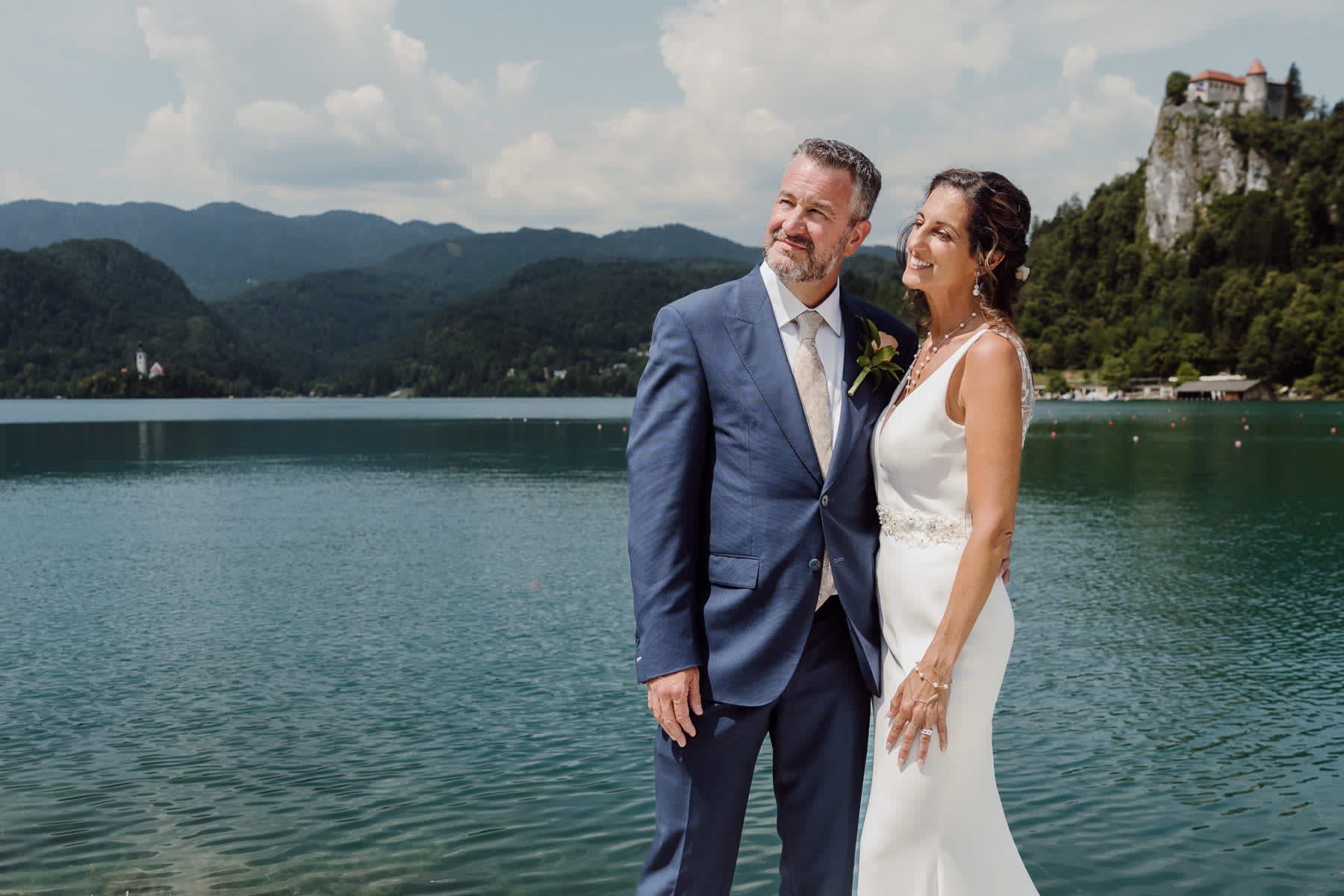 Bride and groom standing by Lake Bled with the castle in the distance.