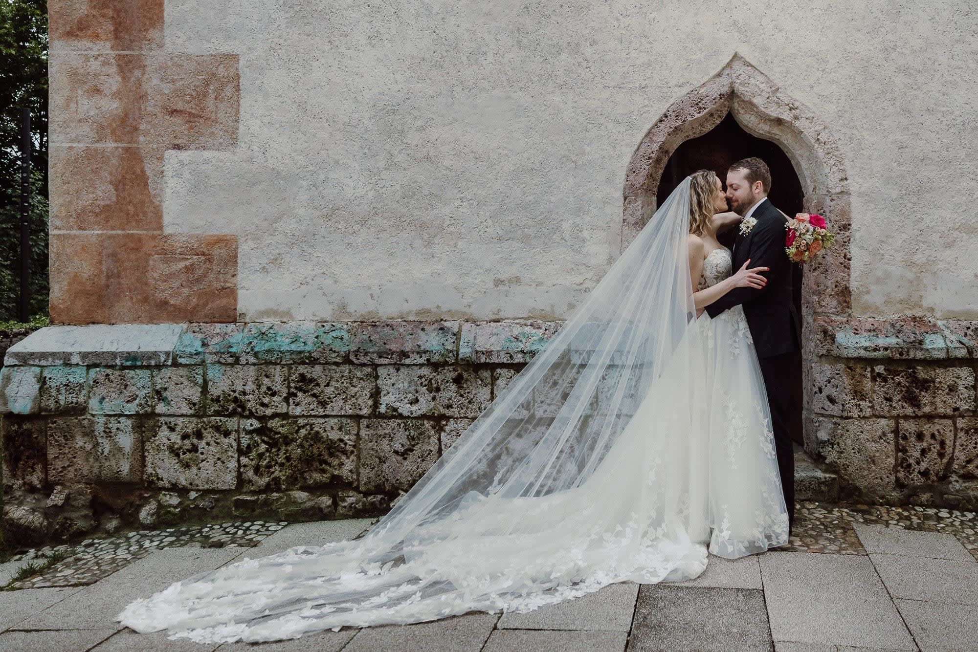 Formal ceremonial portrait beneath a stone arch on Bled Island, with a long veil flowing across the ground.