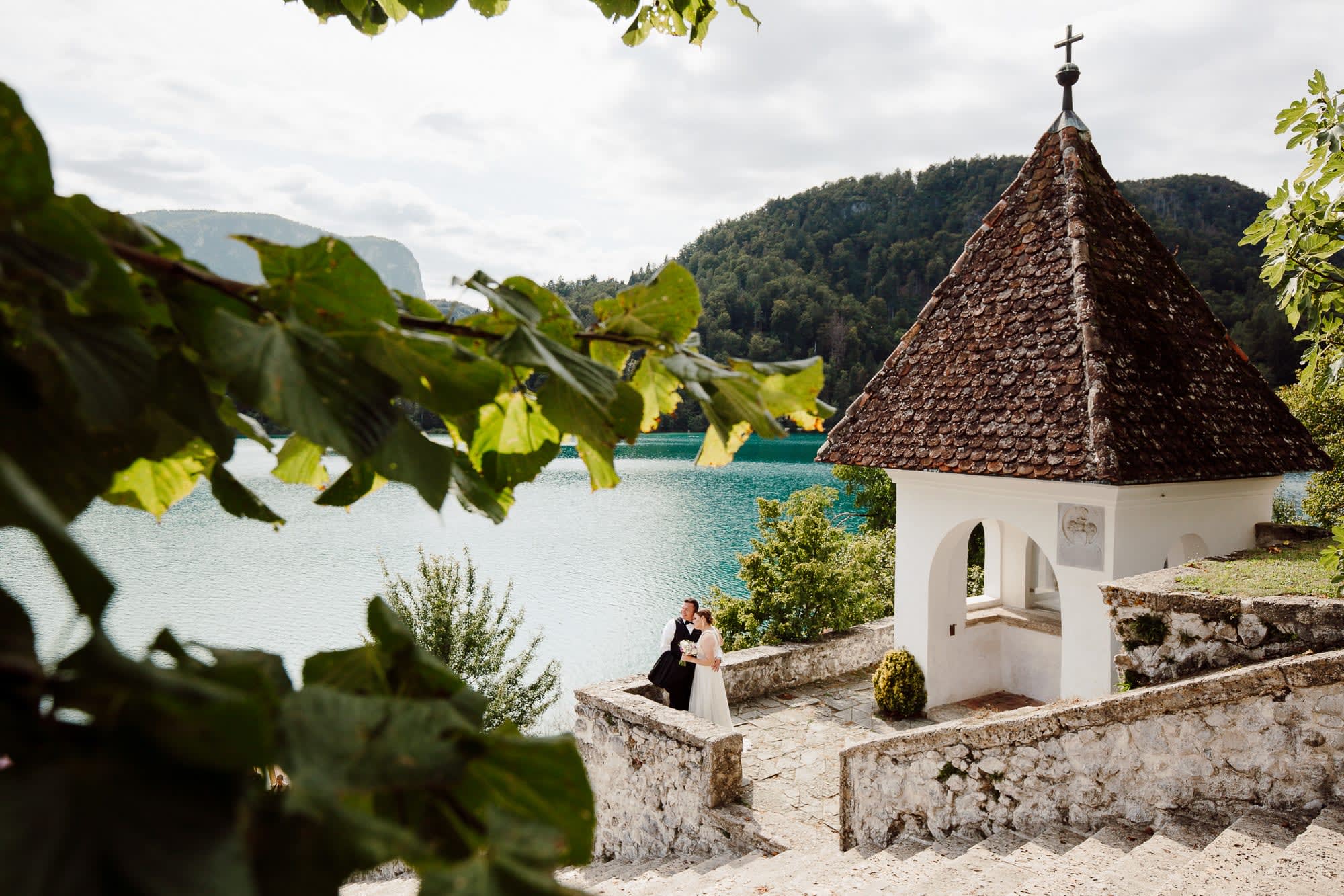 A bride and groom photographed in a peaceful stone courtyard on Bled Island, framed by the lake and historic architecture.