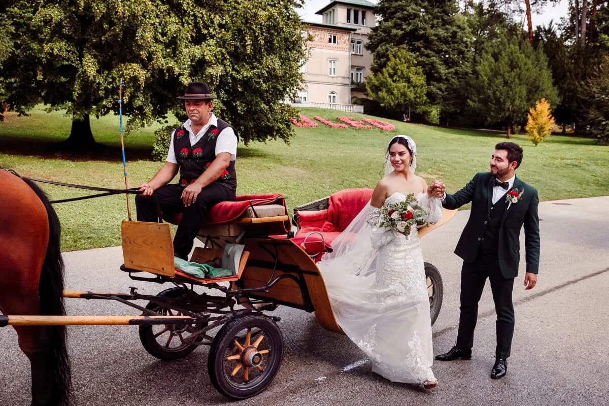 A bride and groom smiling as they take a horse-drawn carriage ride, with the bride holding a bouquet of flowers.
