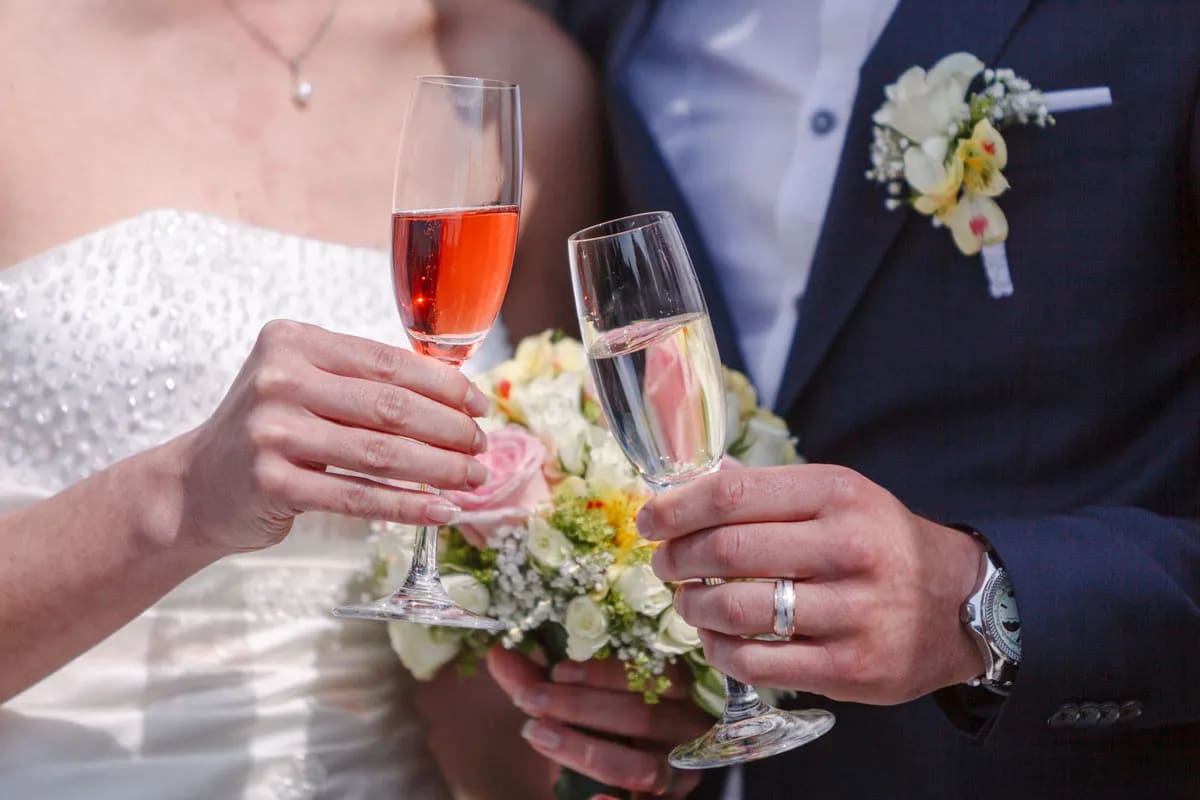 A close-up of a bride and groom toasting with champagne glasses, the bride holding a bouquet of flowers.