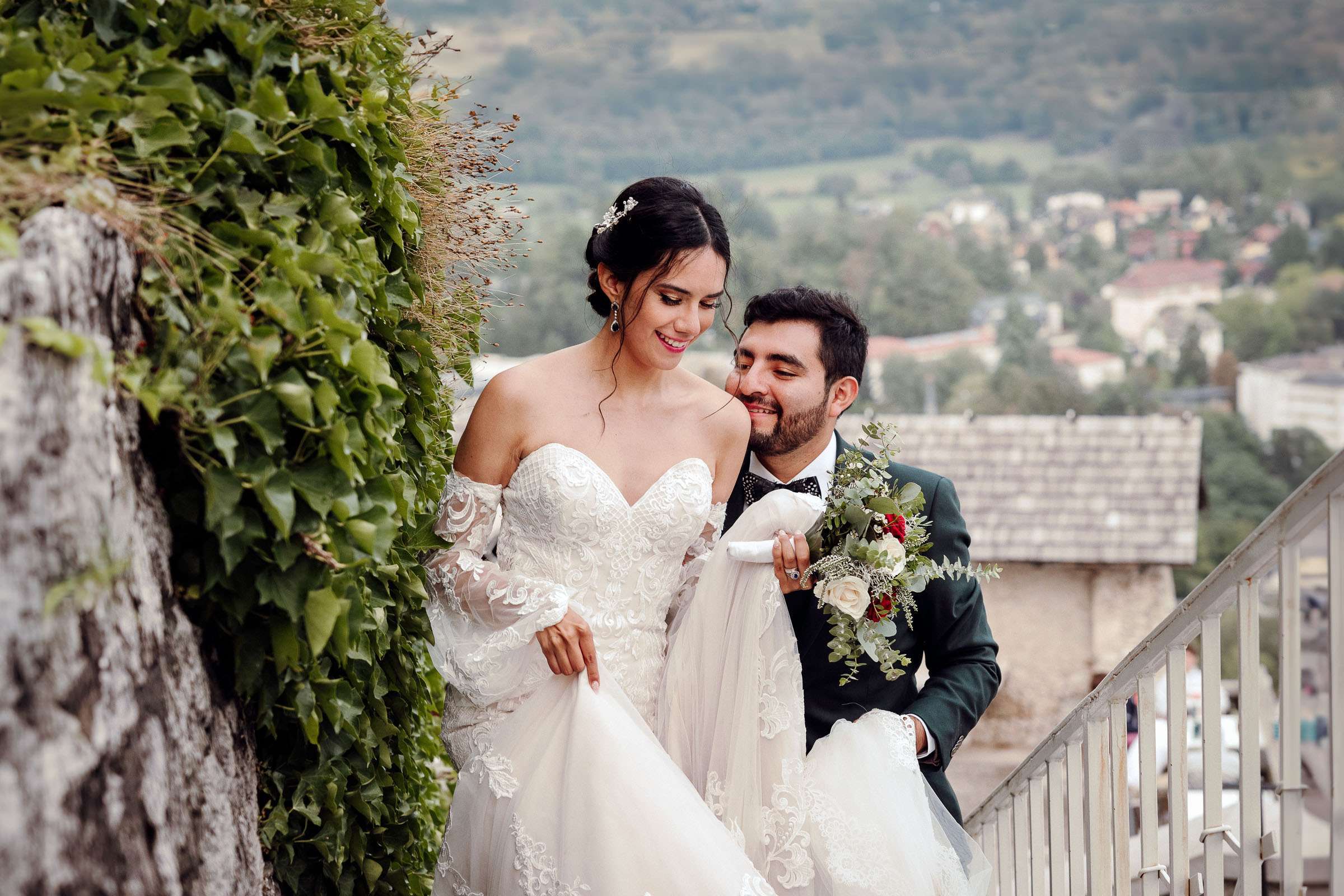 A bride and groom walking up stairs beside an ivy-covered wall, smiling at each other lovingly.