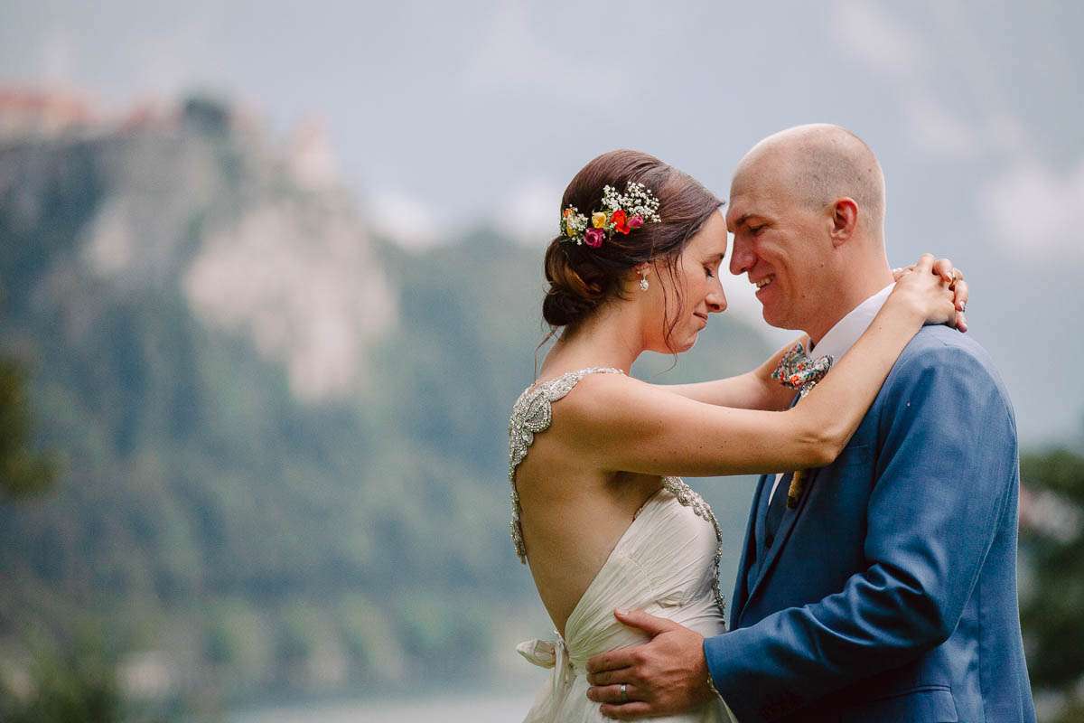 A bride and groom lovingly embrace with a scenic view of a castle and lake in the background.