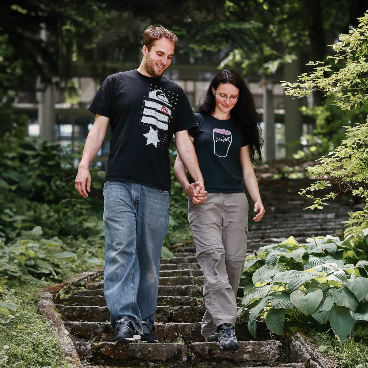 A couple holding hands and walking down a stone path surrounded by lush greenery in a forest setting in Vila Bled.