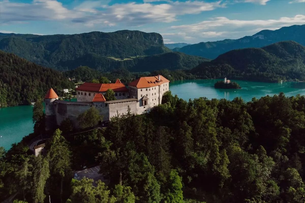 A scenic view of Lake Bled featuring a castle overlooking the lake, with an island and mountains in the background.