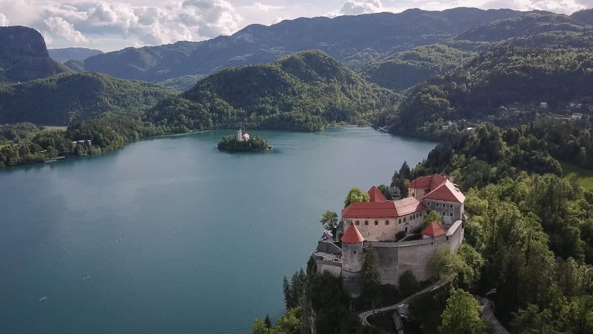 Aerial view of Lake Bled showing the castle and island church surrounded by mountains.