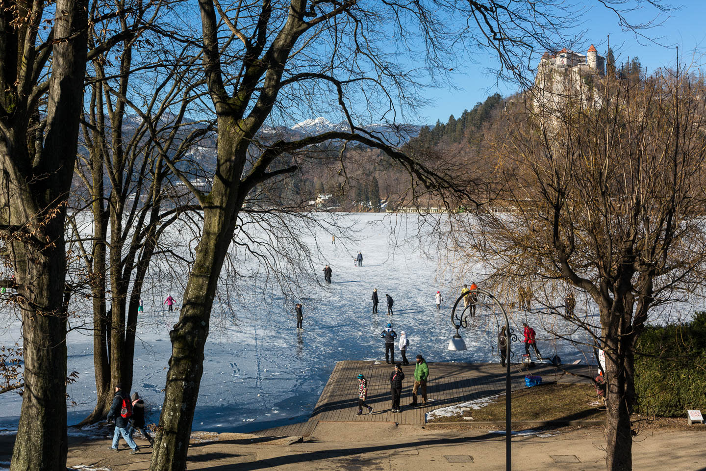 People enjoying winter activities on a frozen lake, with a castle visible in the background at Lake Bled.