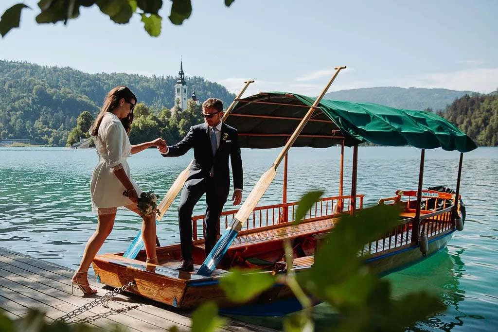 A couple by a traditional boat on Lake Bled, with the church and island in the background.