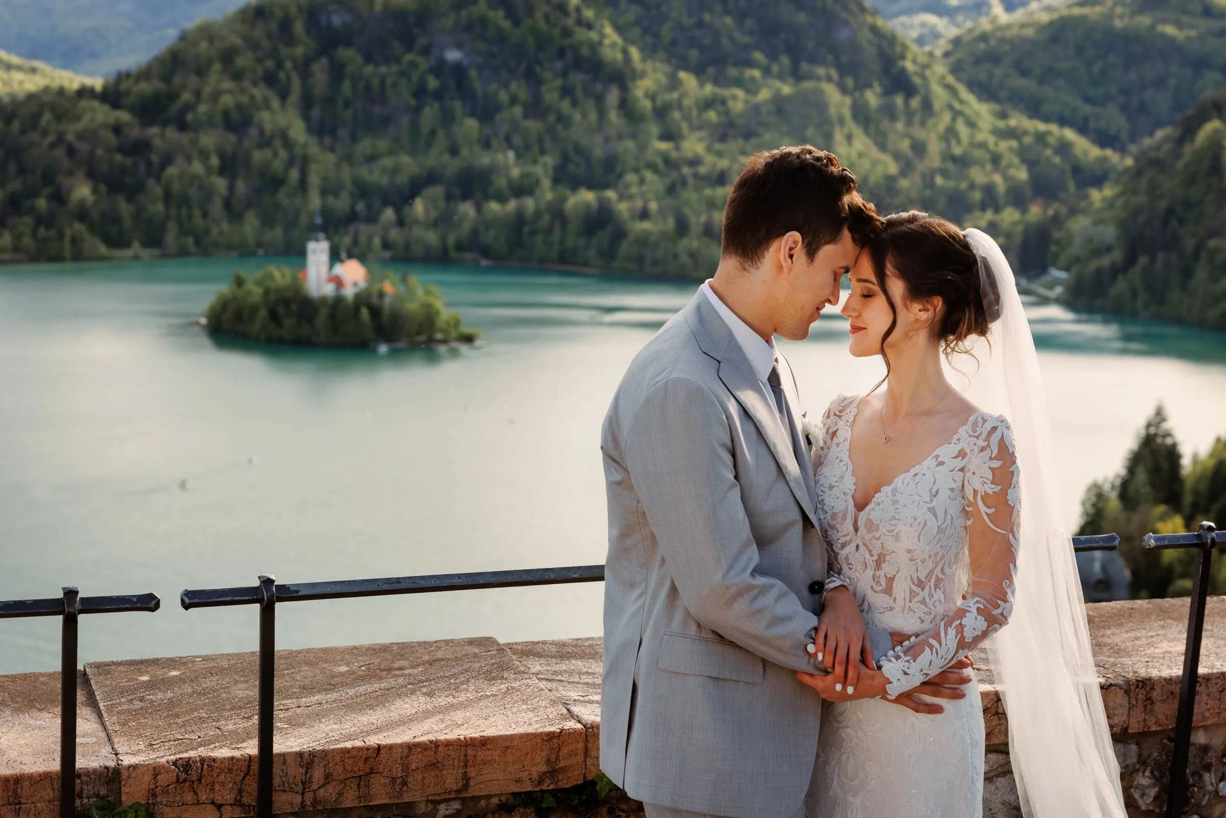 A bride and groom embracing with a view of Lake Bled and the island church in the background.