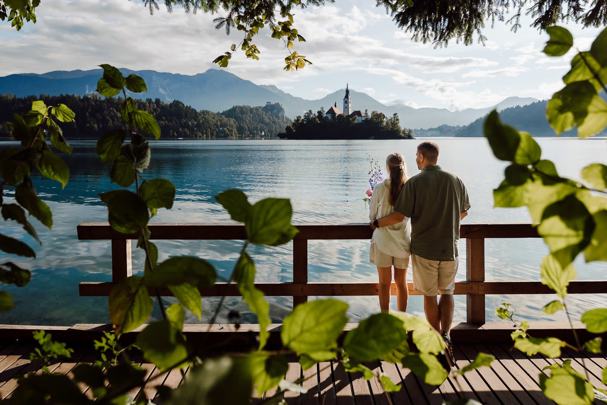 Couple standing on a wooden boardwalk overlooking Bled Island at Lake Bled.