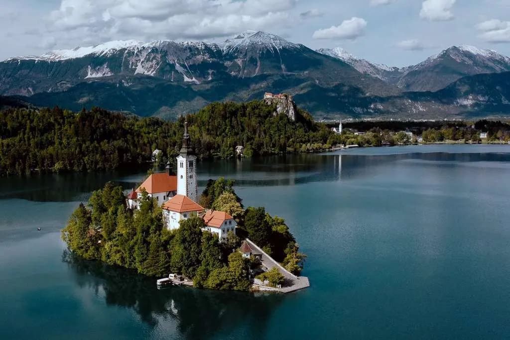 An aerial view of Lake Bled, featuring the iconic island with the church, surrounded by serene waters and majestic mountains in the background.