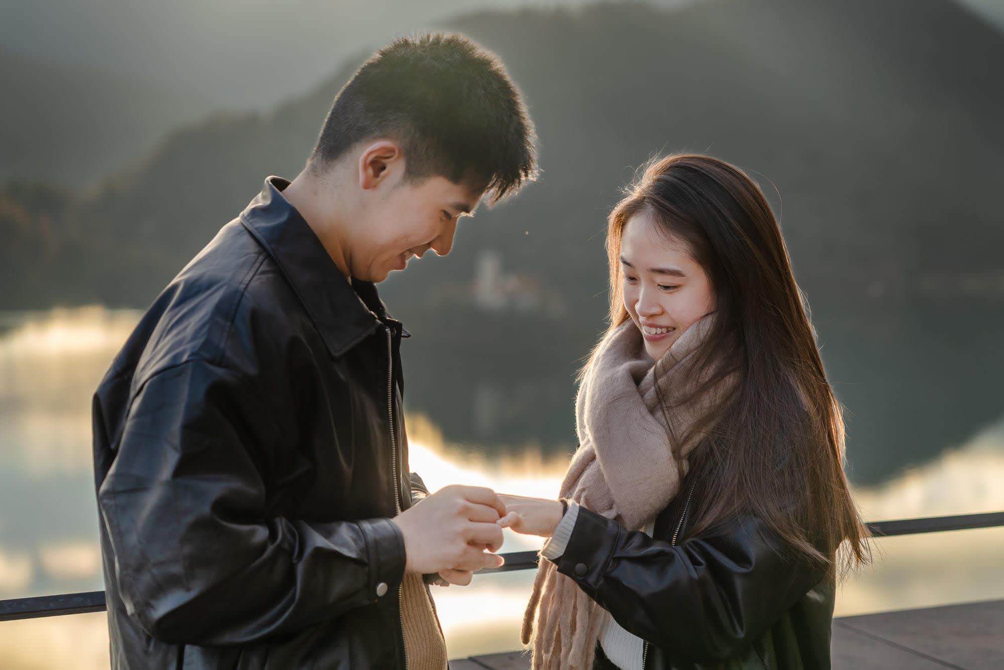 Man placing the engagement ring on his partner's finger after a proposal at Lake Bled.