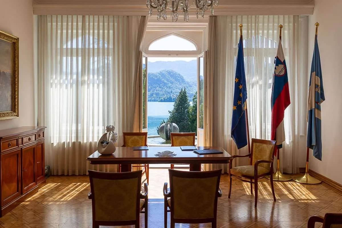 An elegantly furnished room with flags and large windows overlooking Lake Bled, creating a picturesque view.