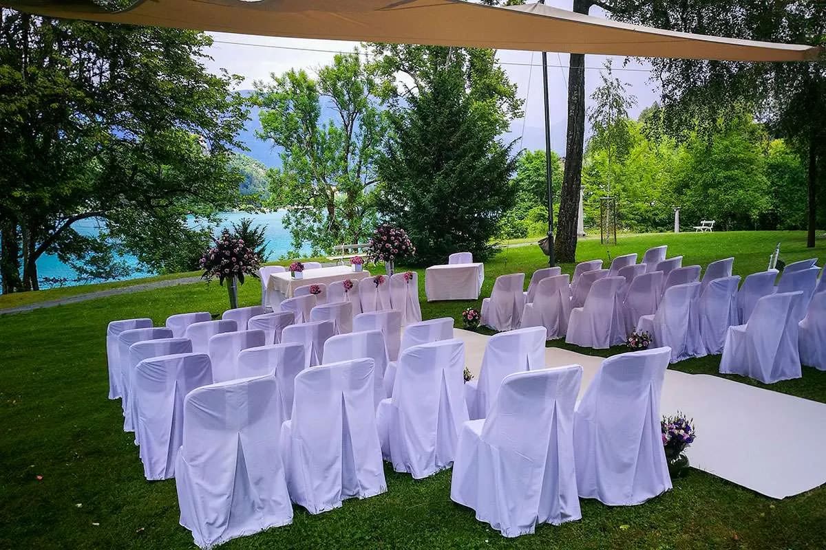 A wedding ceremony setup in Vila Bled with white chairs facing an altar adorned with flowers, under a canopy, with a view of Lake Bled in the background.