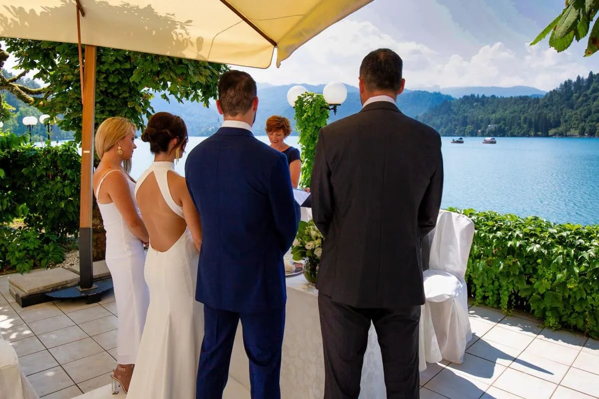 A wedding ceremony taking place by Lake Bled, with a view of the blue lake and surrounding mountains.