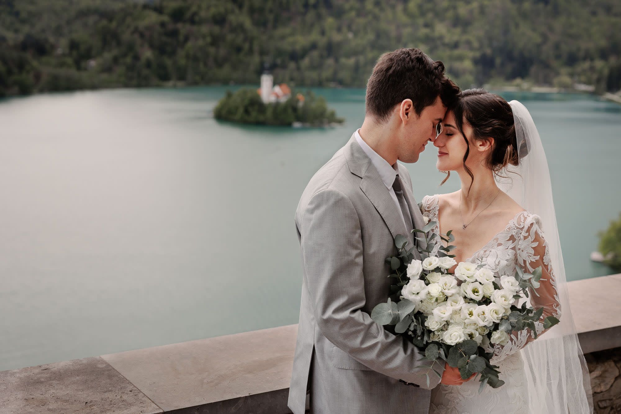 Bride and groom embracing with Lake Bled island in the background, photographed by a Lake Bled wedding photographer.