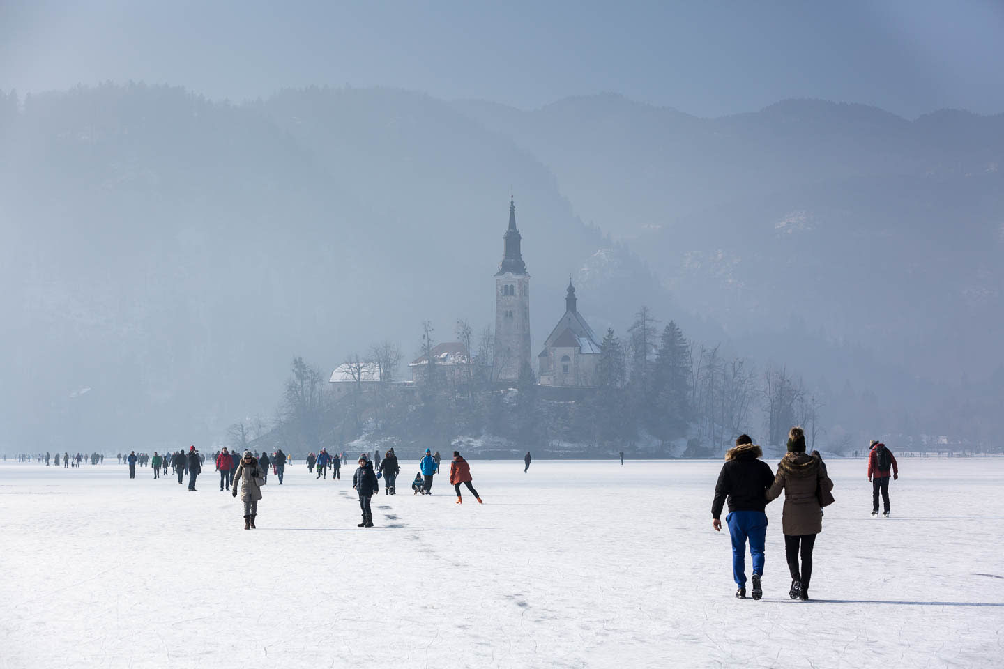 People walking on a frozen lake with a misty view of a church on an island in the distance at Lake Bled.