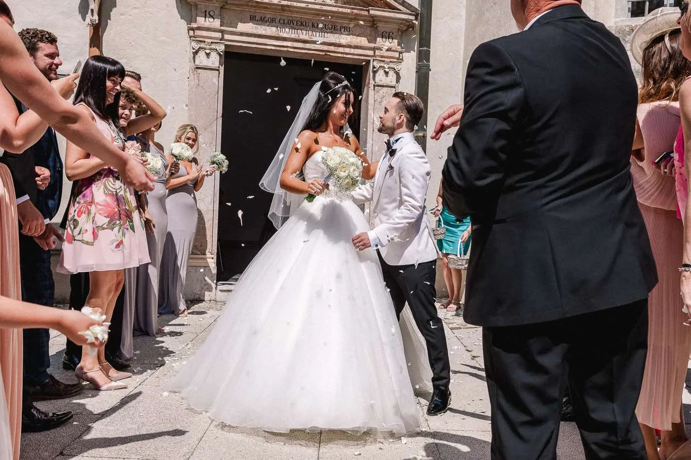A bride and groom stand together happily as guests throw confetti during their wedding ceremony.