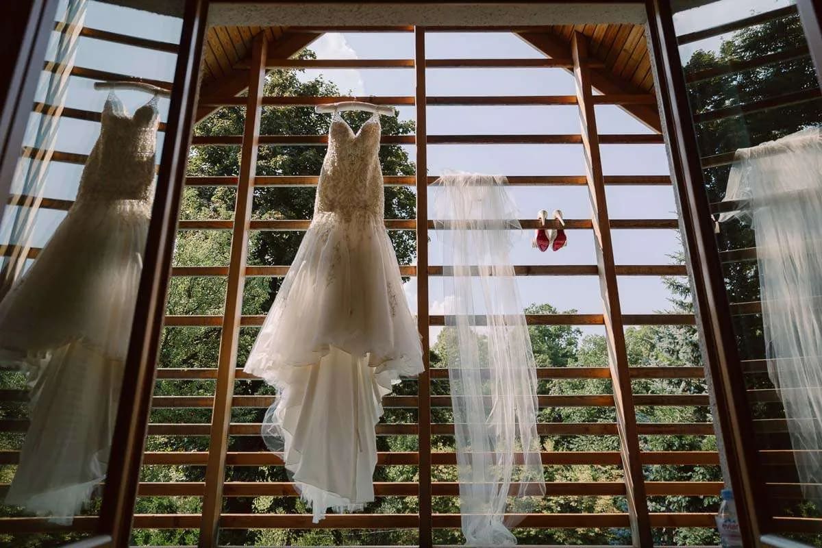 A wedding dress and veil hanging in front of a large window with trees visible in the background.